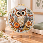 Owl among autumn blooms embroidery kit finished hoop displayed on a wooden stand as cosy tabletop decor