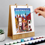 Hand adding finishing details to a German old town painting on a wooden desk calendar