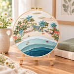 Pastel beach coast embroidery kit finished hoop displayed on a wooden stand as cosy tabletop decor