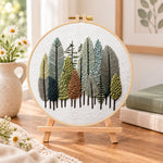 Pastel forest grove embroidery kit finished hoop displayed on a wooden stand as cosy tabletop decor