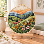 Pastel mountain flower hills embroidery kit finished hoop displayed on a wooden stand as cozy tabletop decor