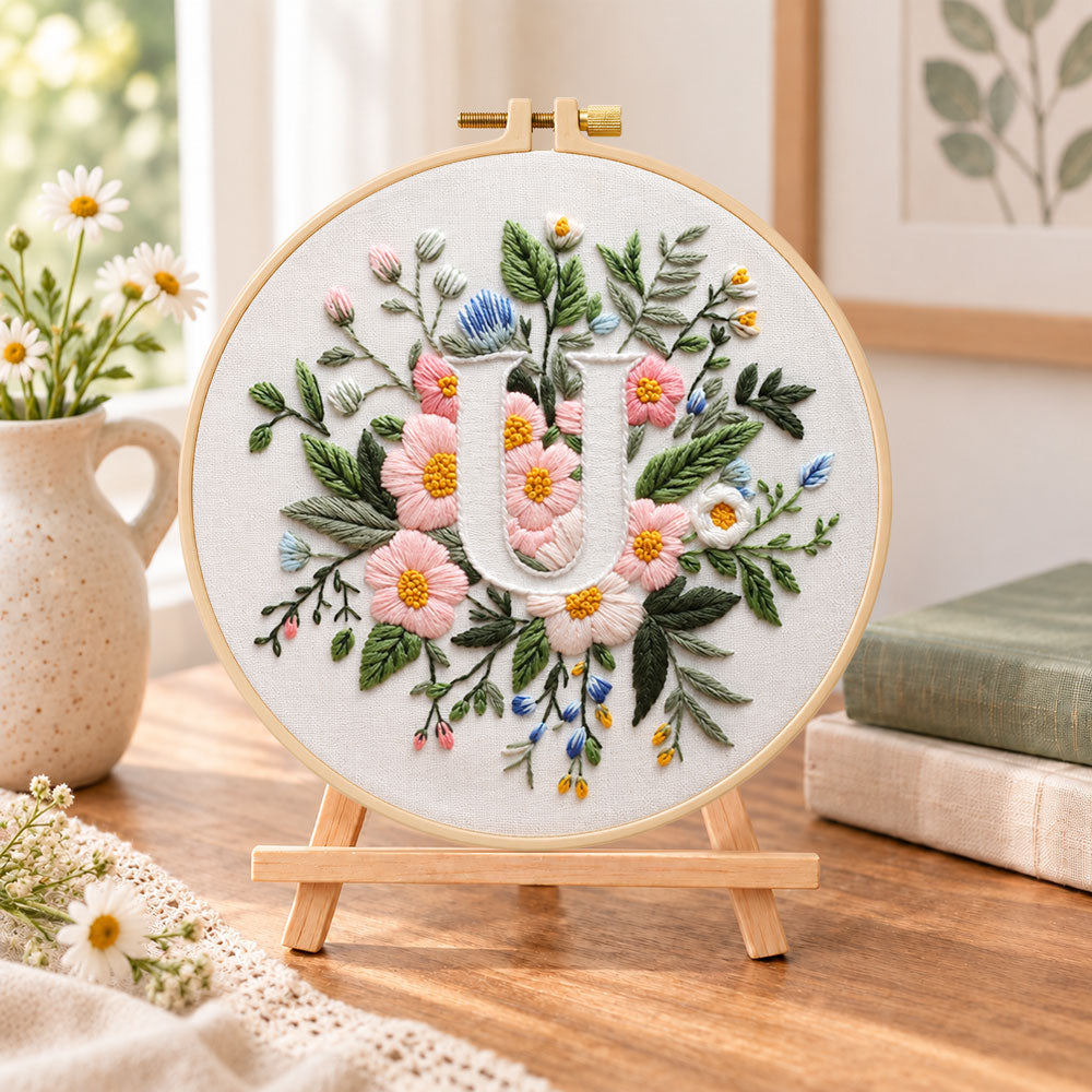 Pastel pink blooms and letter u embroidery kit finished hoop displayed on a wooden stand as cosy tabletop decor