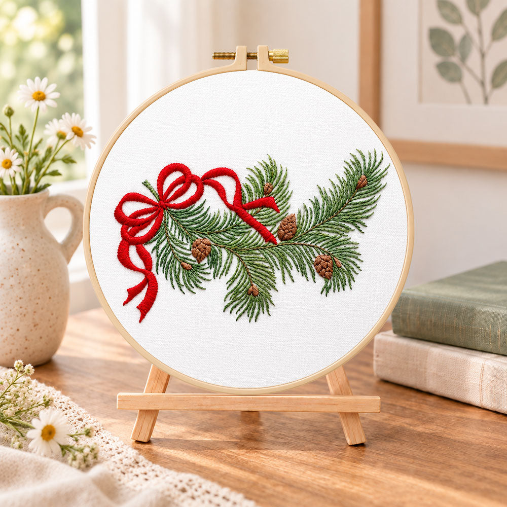 Pine branch with bow embroidery kit finished hoop displayed on a wooden stand as cozy tabletop decor