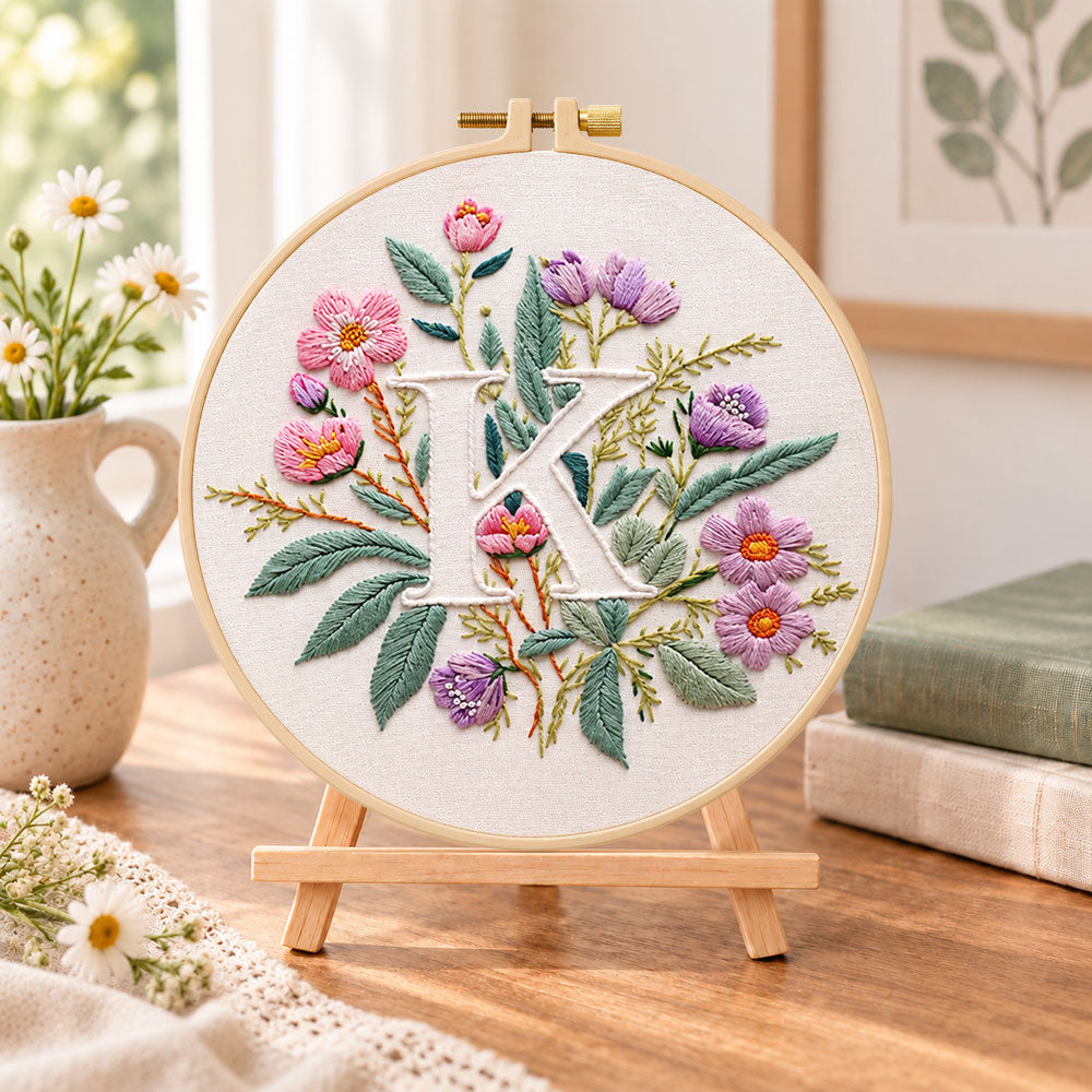 Pink blooms and letter k embroidery kit finished hoop displayed on a wooden stand as cosy tabletop decor