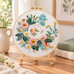 Pink botanical blooms and letter c embroidery kit finished hoop displayed on a wooden stand as cosy tabletop decor
