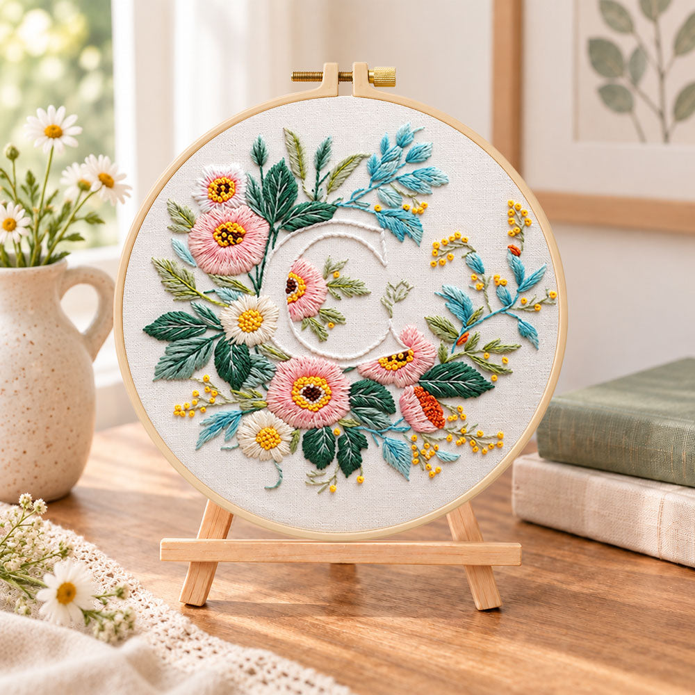 Pink botanical blooms and letter c embroidery kit finished hoop displayed on a wooden stand as cosy tabletop decor