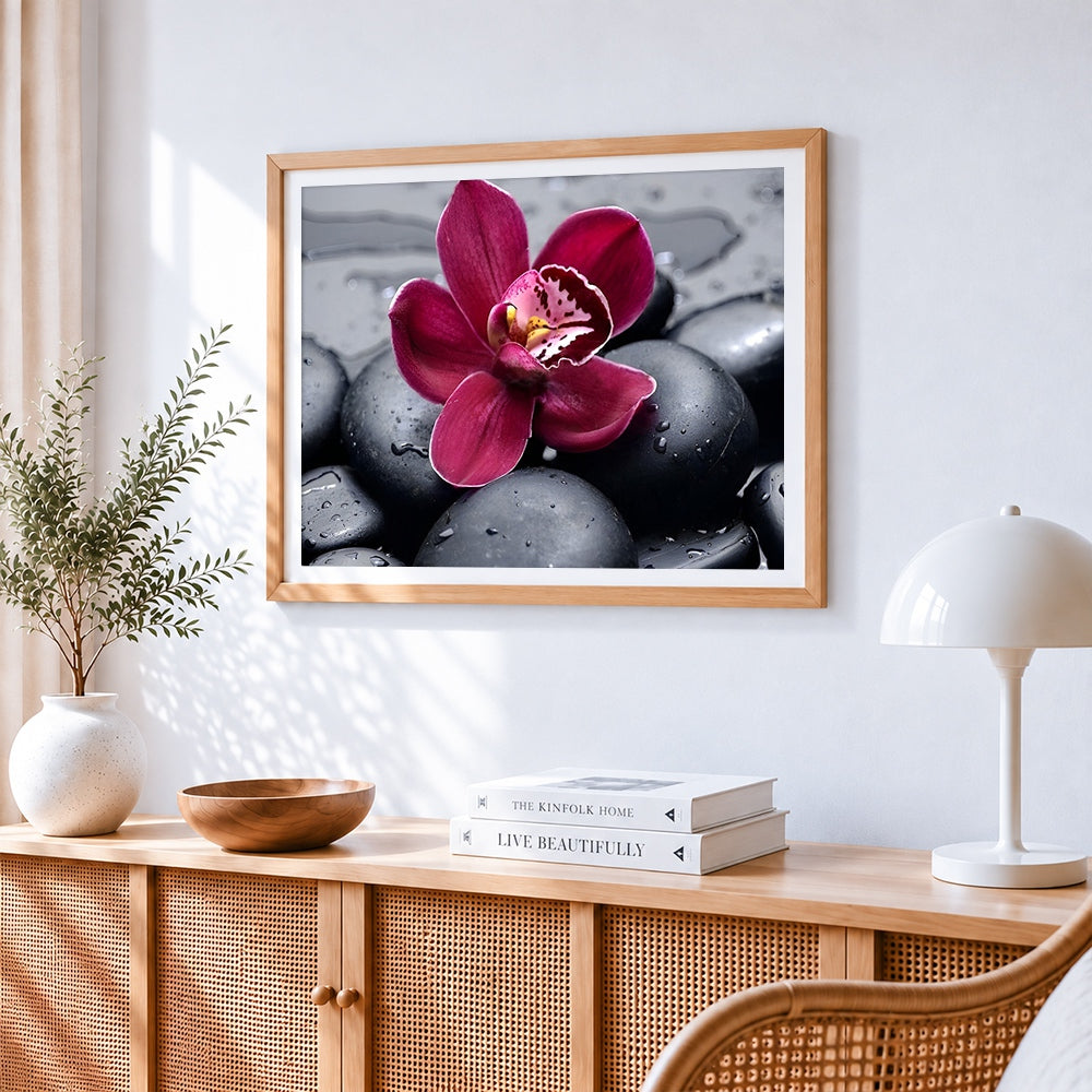 Pink orchid on black pebbles cross stitch artwork displayed on wall as home decor