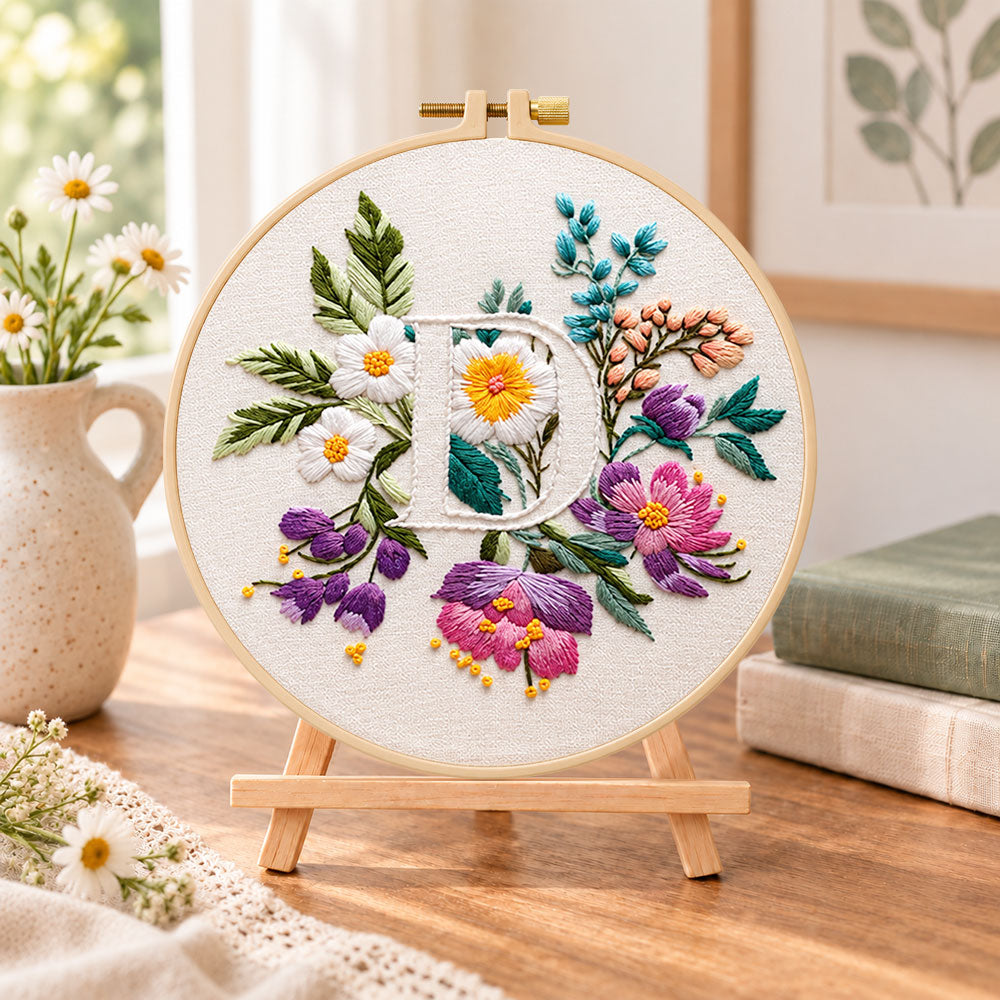 Purple daisy garden and letter d embroidery kit finished hoop displayed on a wooden stand as cosy tabletop decor