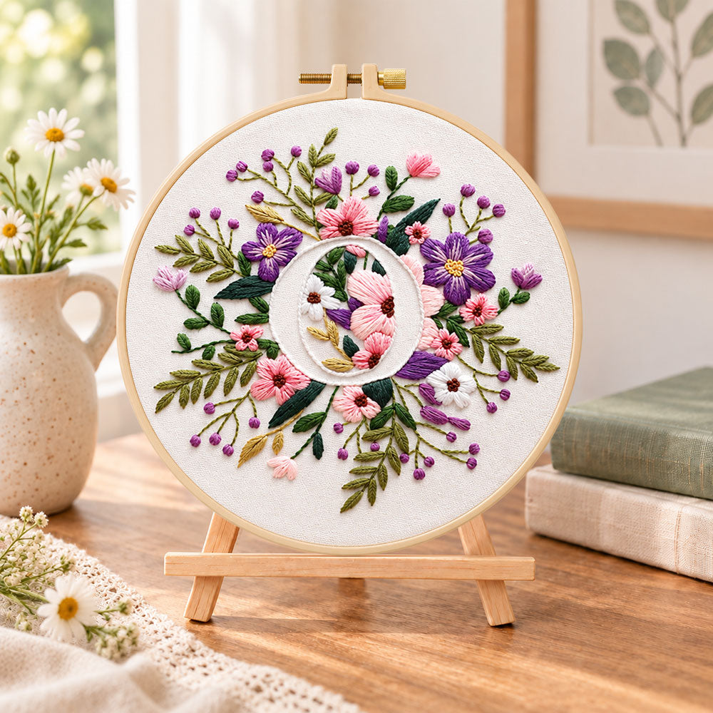 Purple floral ring and letter o embroidery kit finished hoop displayed on a wooden stand as cosy tabletop decor
