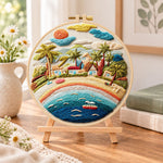 Rainbow seaside village embroidery kit finished hoop displayed on a wooden stand as cosy tabletop decor