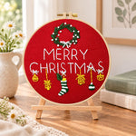 Red christmas greeting embroidery kit finished hoop displayed on a wooden stand as cozy tabletop decor