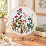 Red wildflower bouquet embroidery kit finished hoop displayed on a wooden stand as cosy tabletop decor