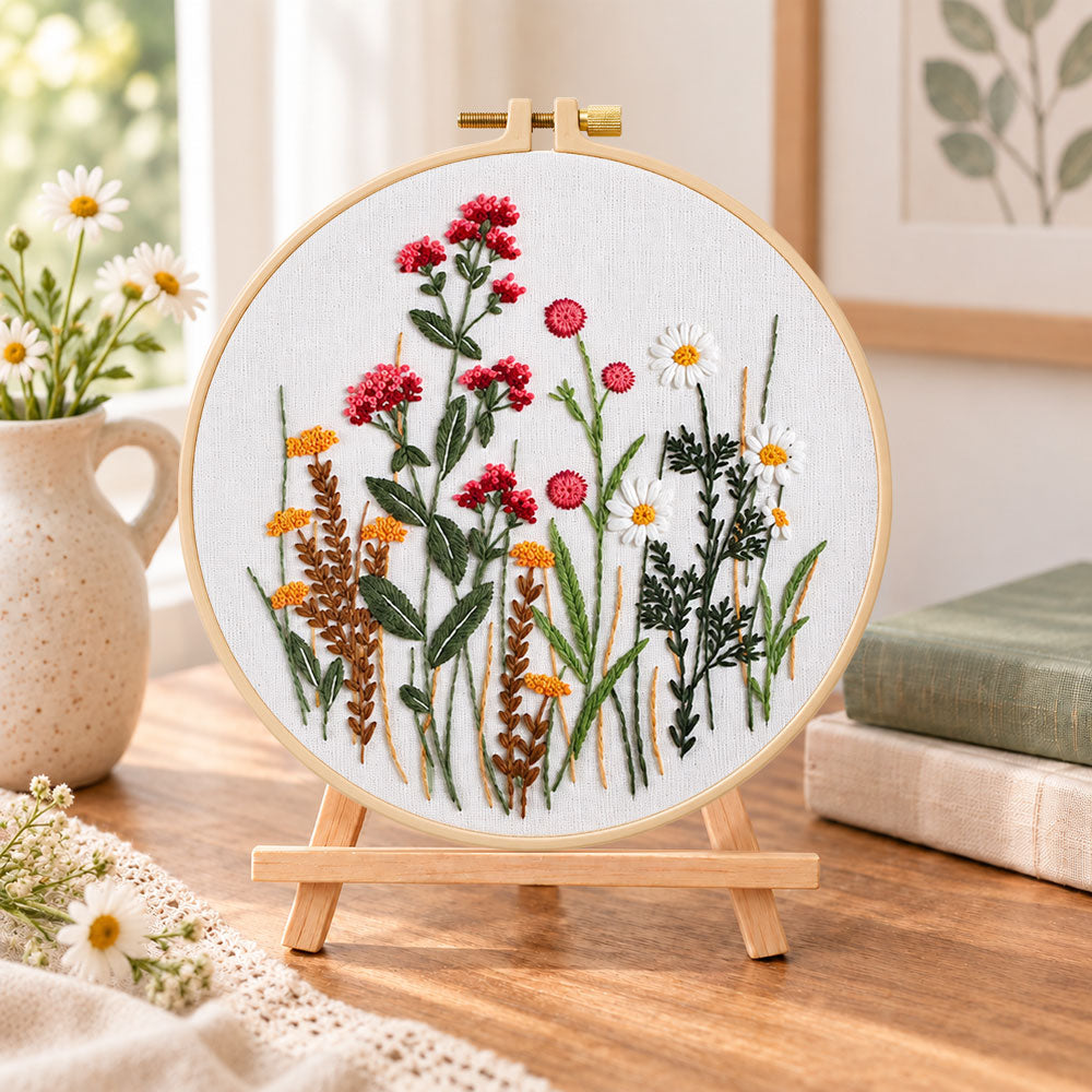 Red wildflower bouquet embroidery kit finished hoop displayed on a wooden stand as cosy tabletop decor