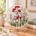 Red wildflower patch embroidery kit finished hoop displayed on a wooden stand as cosy tabletop decor