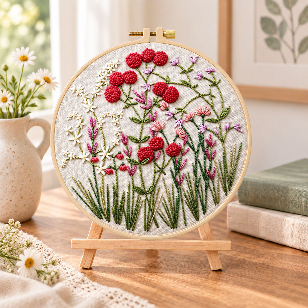 Red wildflower patch embroidery kit finished hoop displayed on a wooden stand as cosy tabletop decor