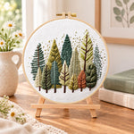Rustic pine tree grove embroidery kit finished hoop displayed on a wooden stand as cosy tabletop decor