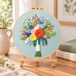 Sage green floral bouquet embroidery kit finished hoop displayed on a wooden stand as cosy tabletop decor