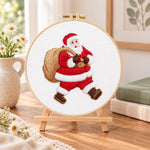 Santa with gift sack embroidery kit finished hoop displayed on a wooden stand as cozy tabletop decor