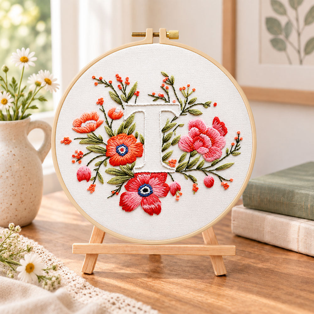 Scarlet florals and letter t embroidery kit finished hoop displayed on a wooden stand as cosy tabletop decor