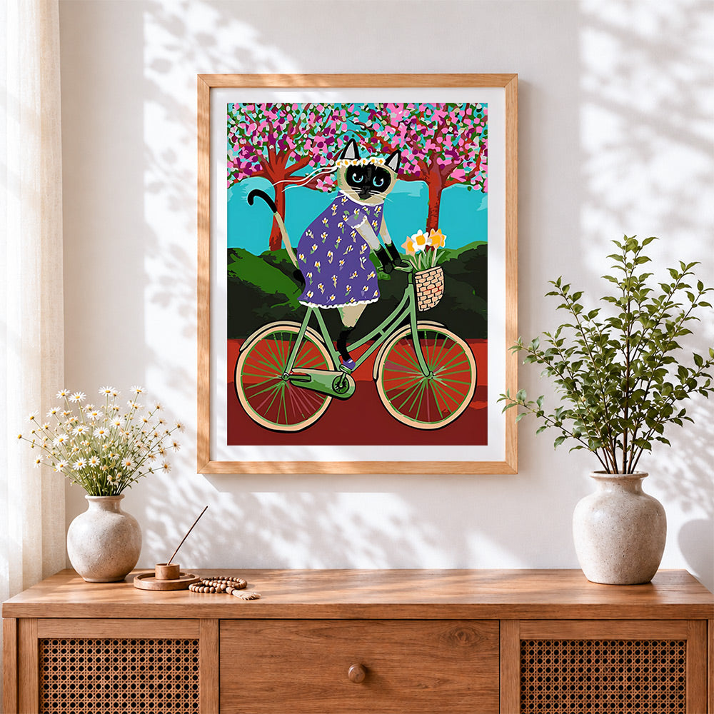 Finished siamese cat riding a bicycle cross stitch artwork displayed
