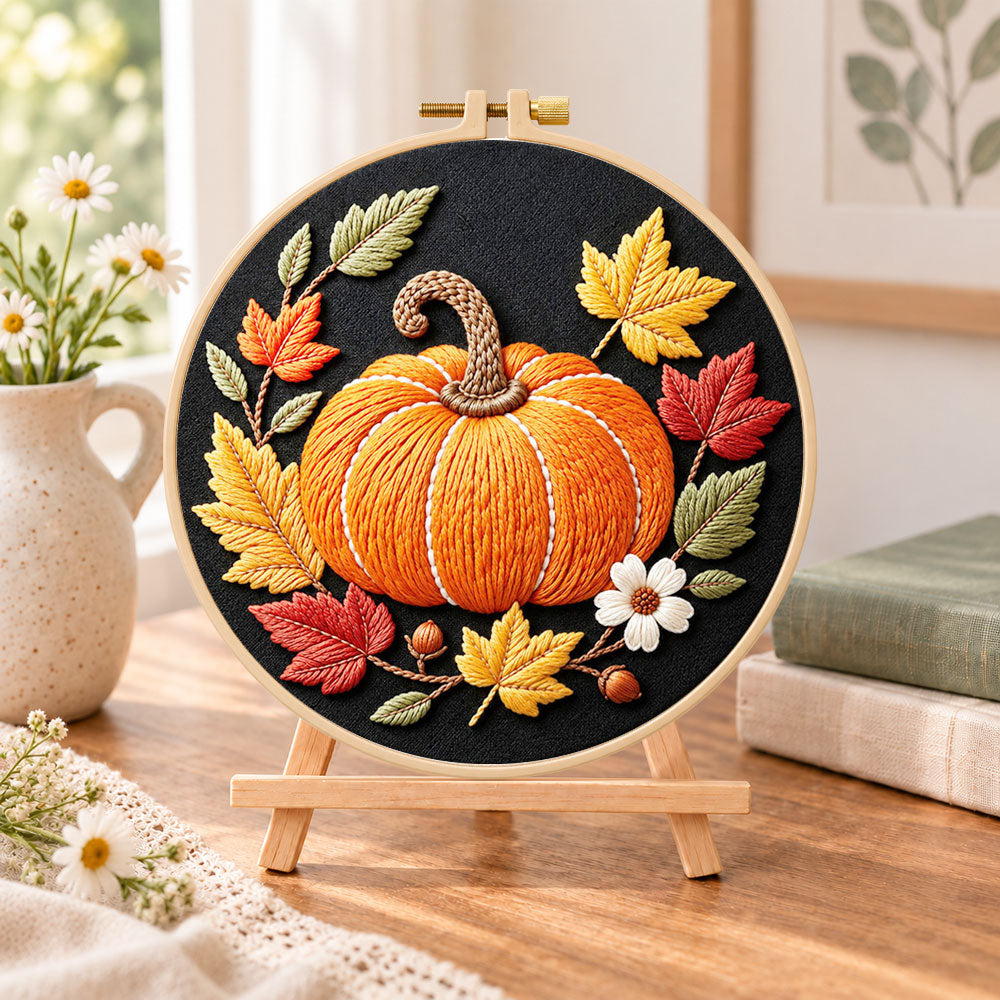 Single pumpkin on black fabric embroidery kit finished hoop displayed on a wooden stand as cosy tabletop decor