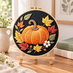 Single pumpkin on black fabric embroidery kit finished hoop displayed on a wooden stand as cosy tabletop decor