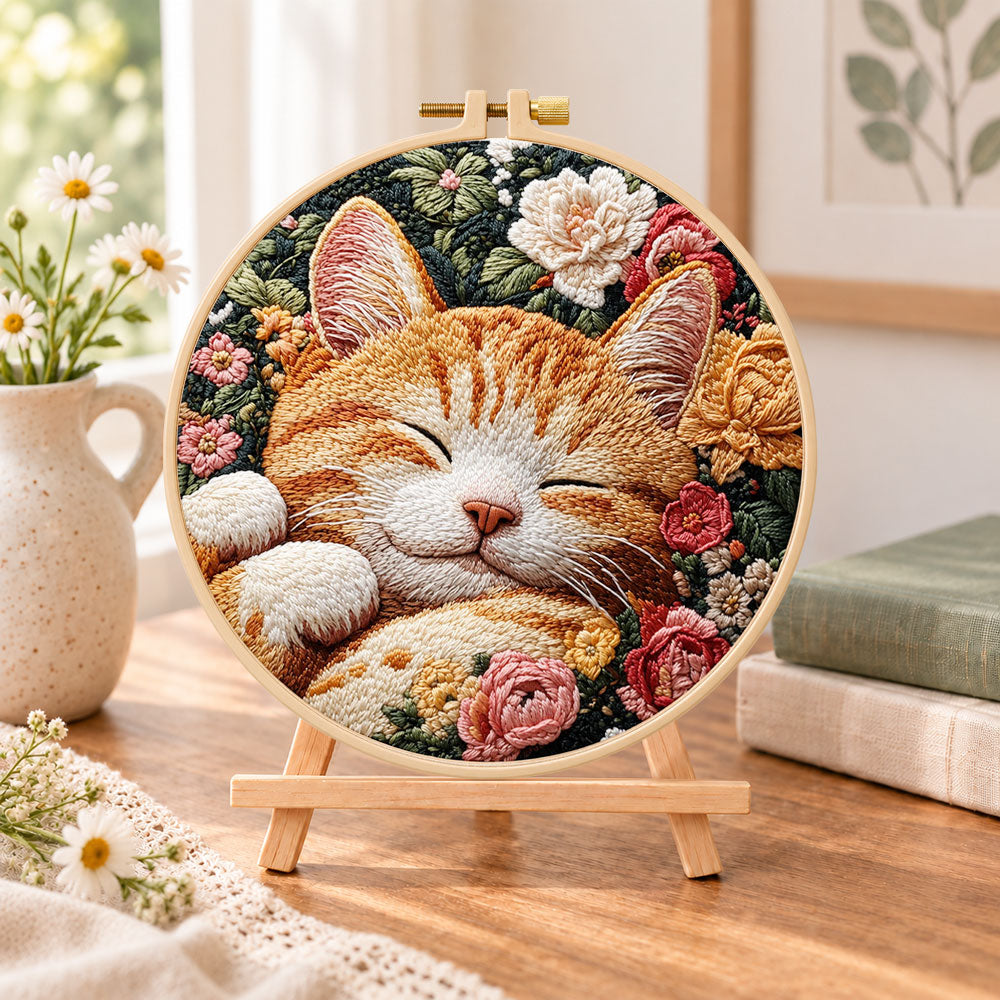 Sleeping ginger cat among roses embroidery kit finished hoop displayed on a wooden stand as cozy tabletop decor