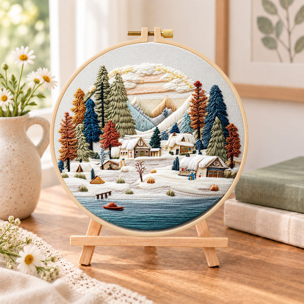 Snow mountain village embroidery kit finished hoop displayed on a wooden stand as cosy tabletop decor