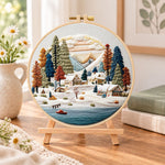 Snow mountain village embroidery kit finished hoop displayed on a wooden stand as cosy tabletop decor