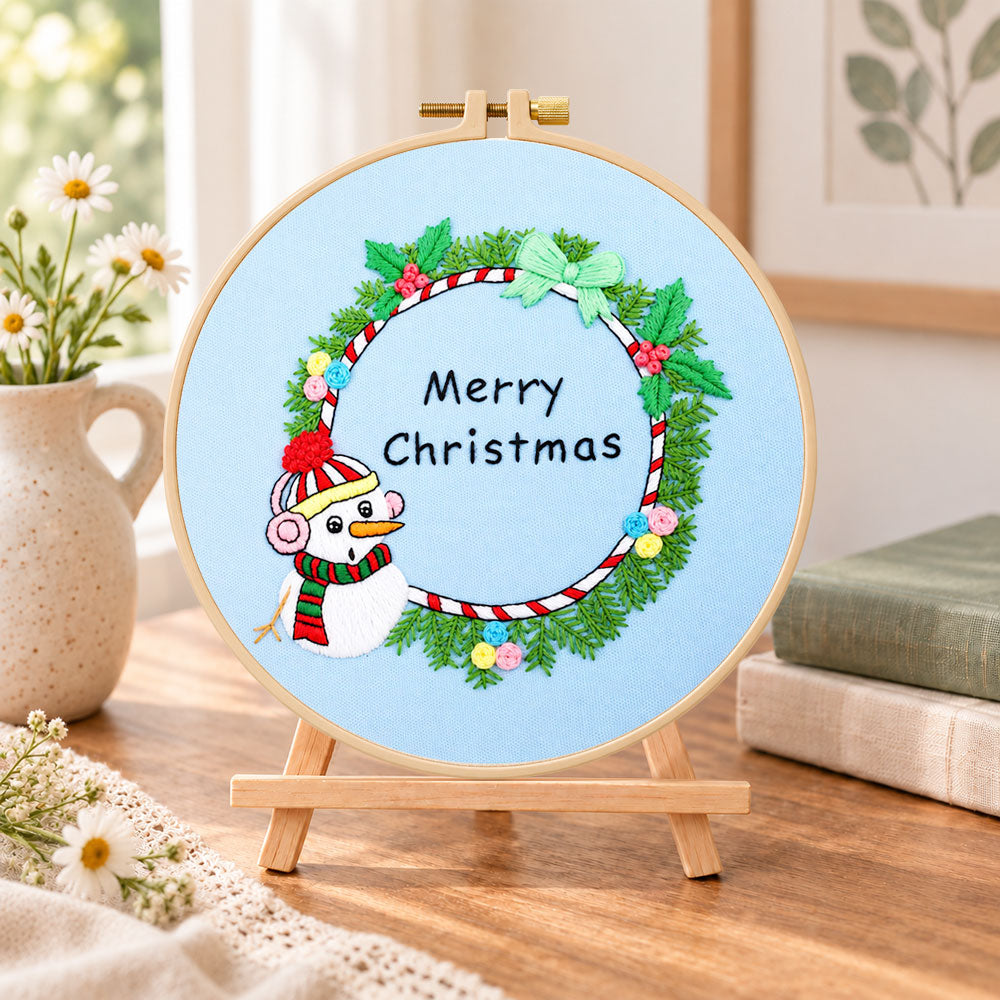 Snowman wreath quote embroidery kit finished hoop displayed on a wooden stand as cosy tabletop decor