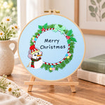 Snowman wreath quote embroidery kit finished hoop displayed on a wooden stand as cosy tabletop decor