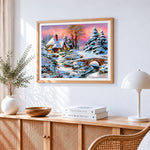 Snowy cottage and bridge at sunset cross stitch artwork displayed on wall as home decor