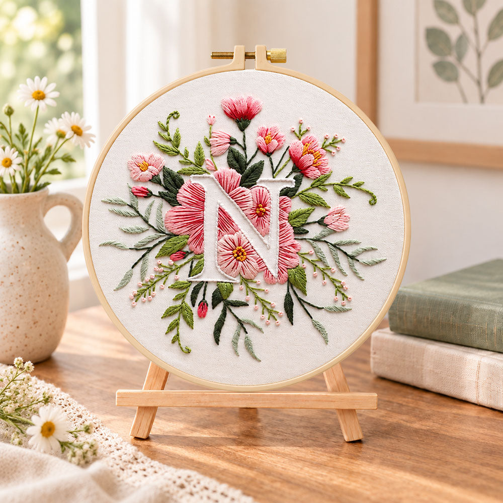 Soft pink petals and letter n embroidery kit finished hoop displayed on a wooden stand as cosy tabletop decor