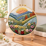 Sunlit mountain wildflowers embroidery kit finished hoop displayed on a wooden stand as cozy tabletop decor