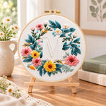 Sunny floral wreath and letter m embroidery kit finished hoop displayed on a wooden stand as cosy tabletop decor