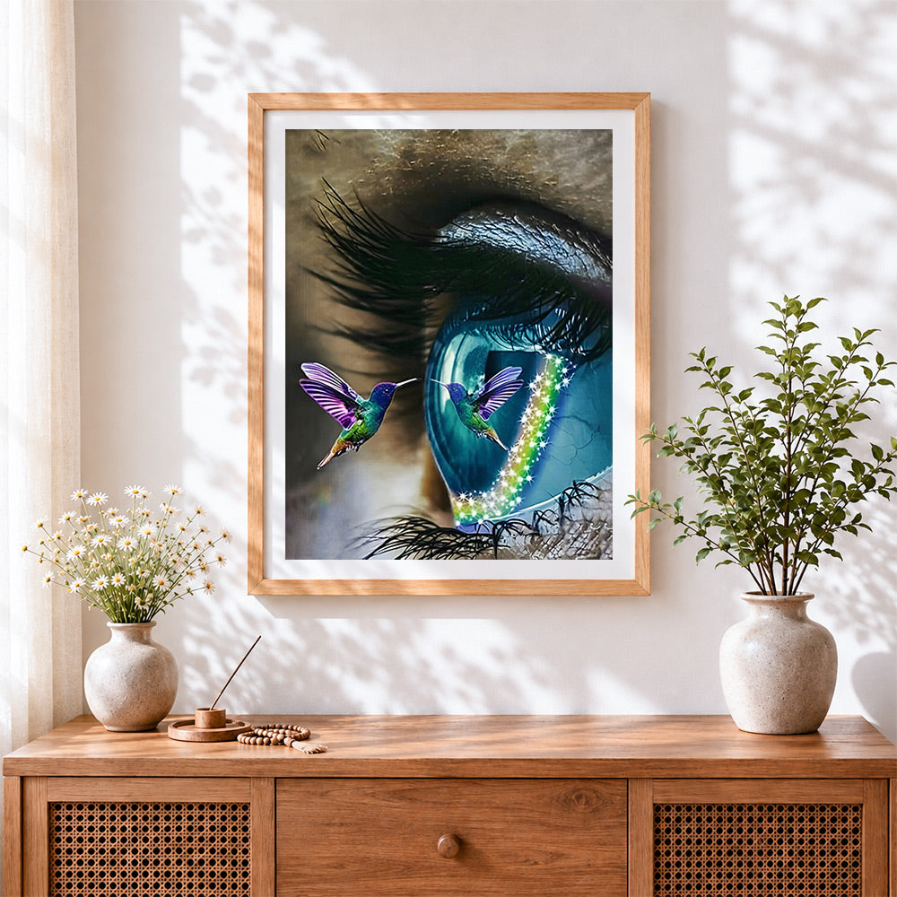Finished surreal blue eye and a hummingbird cross stitch artwork displayed
