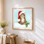 Tabby cat in santa hat with holly cross stitch artwork displayed on wall as home decor
