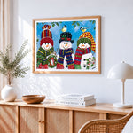 Three cheerful snowmen in knitted hats paint by numbers artwork displayed on wall as home decor