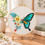 Turquoise butterfly and blooms embroidery kit finished hoop displayed on a wooden stand as cozy tabletop decor