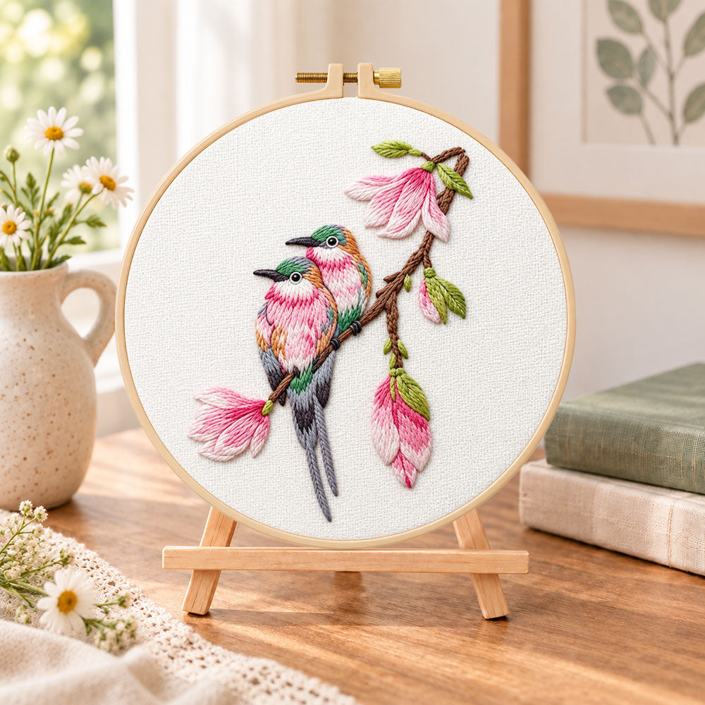Two birds on magnolia branch embroidery kit finished hoop displayed on a wooden stand as cosy tabletop decor