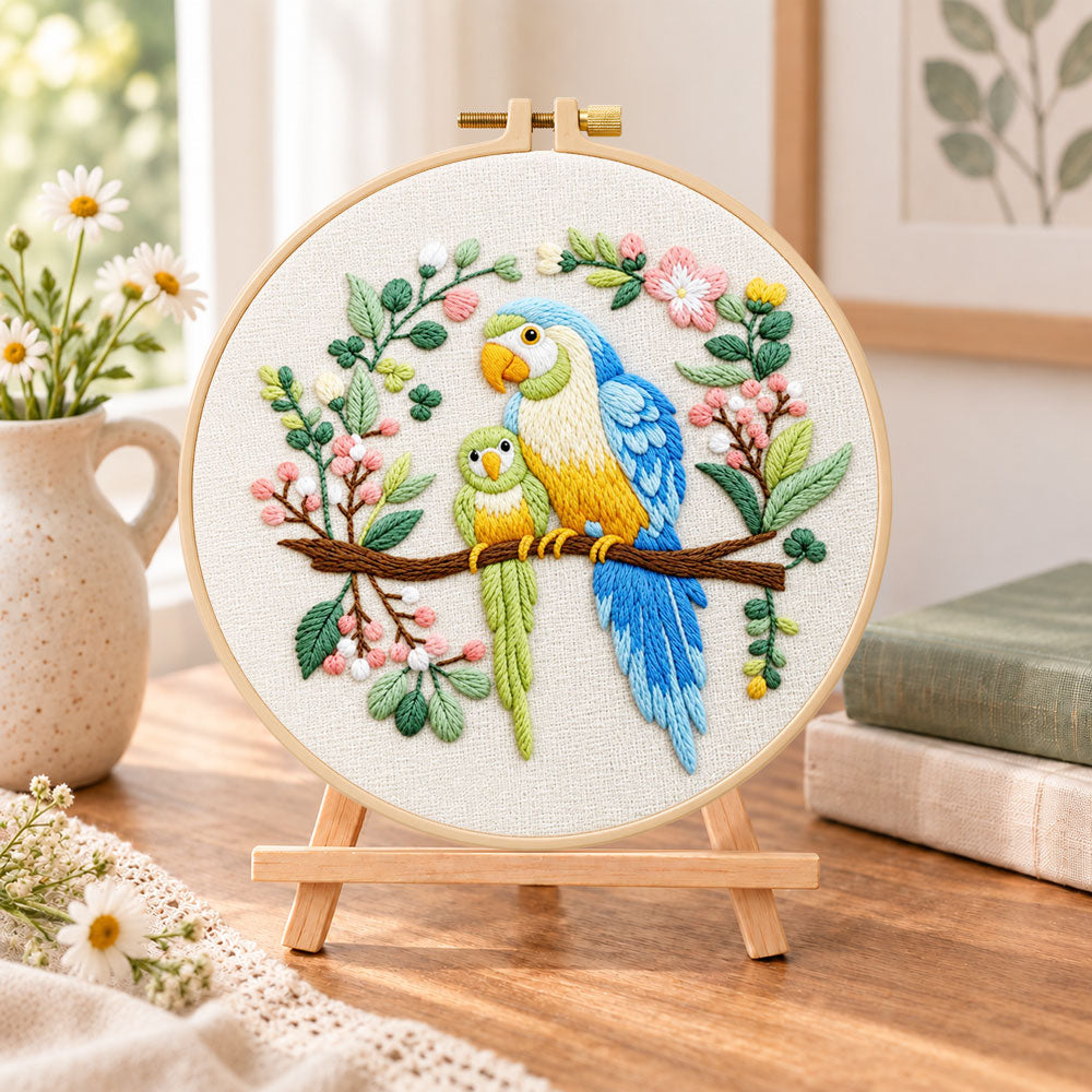 Two parrots on blossom branch embroidery kit finished hoop displayed on a wooden stand as cosy tabletop decor