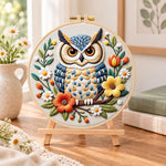 Vibrant floral owl embroidery kit finished hoop displayed on a wooden stand as cosy tabletop decor