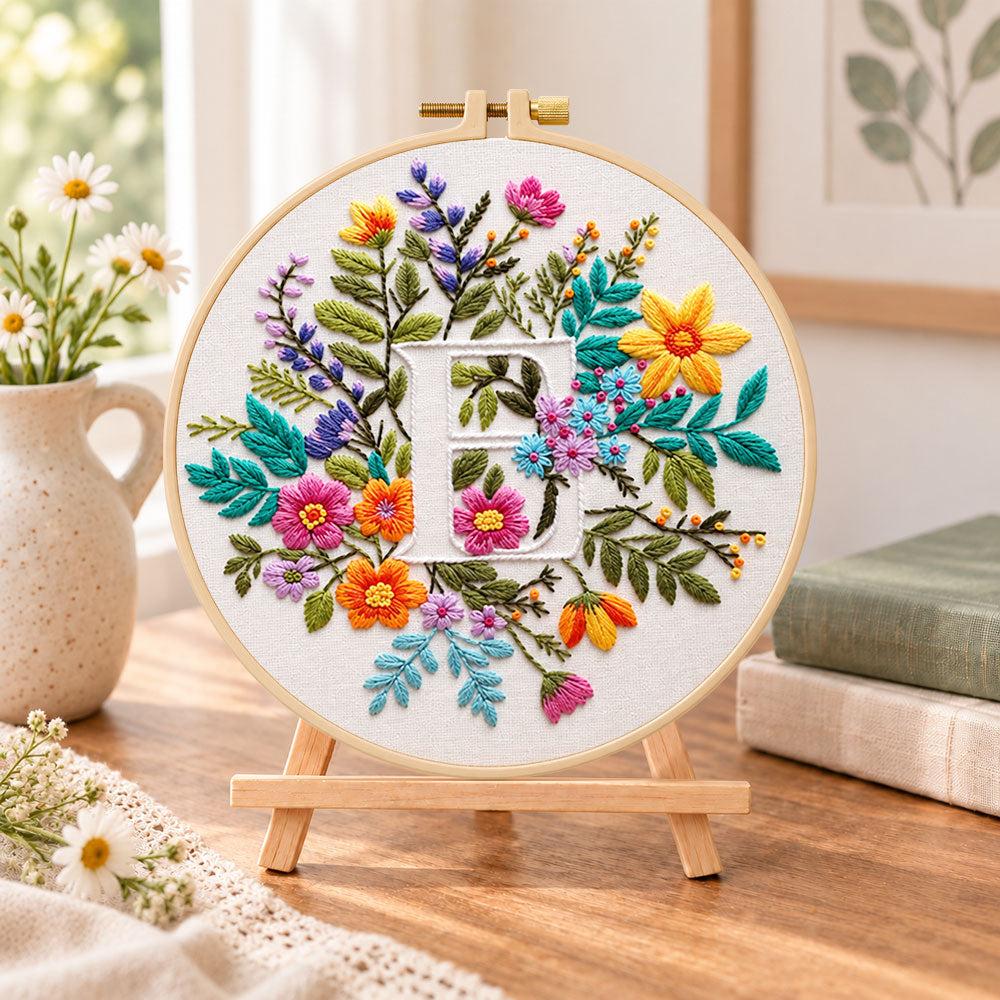 Vibrant wildflowers and letter e embroidery kit finished hoop displayed on a wooden stand as cosy tabletop decor