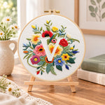 Vibrant wildflowers and letter v embroidery kit finished hoop displayed on a wooden stand as cosy tabletop decor