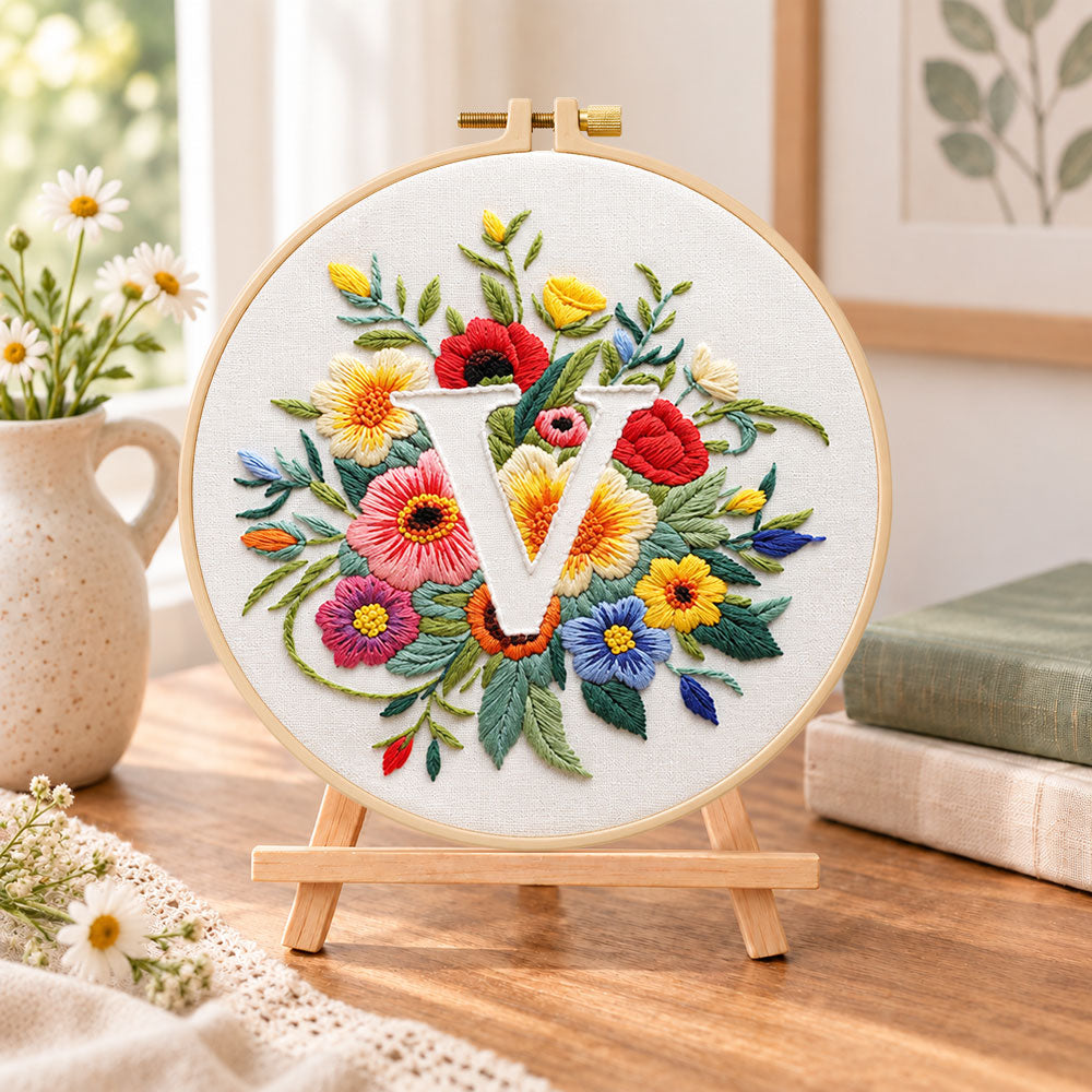 Vibrant wildflowers and letter v embroidery kit finished hoop displayed on a wooden stand as cosy tabletop decor