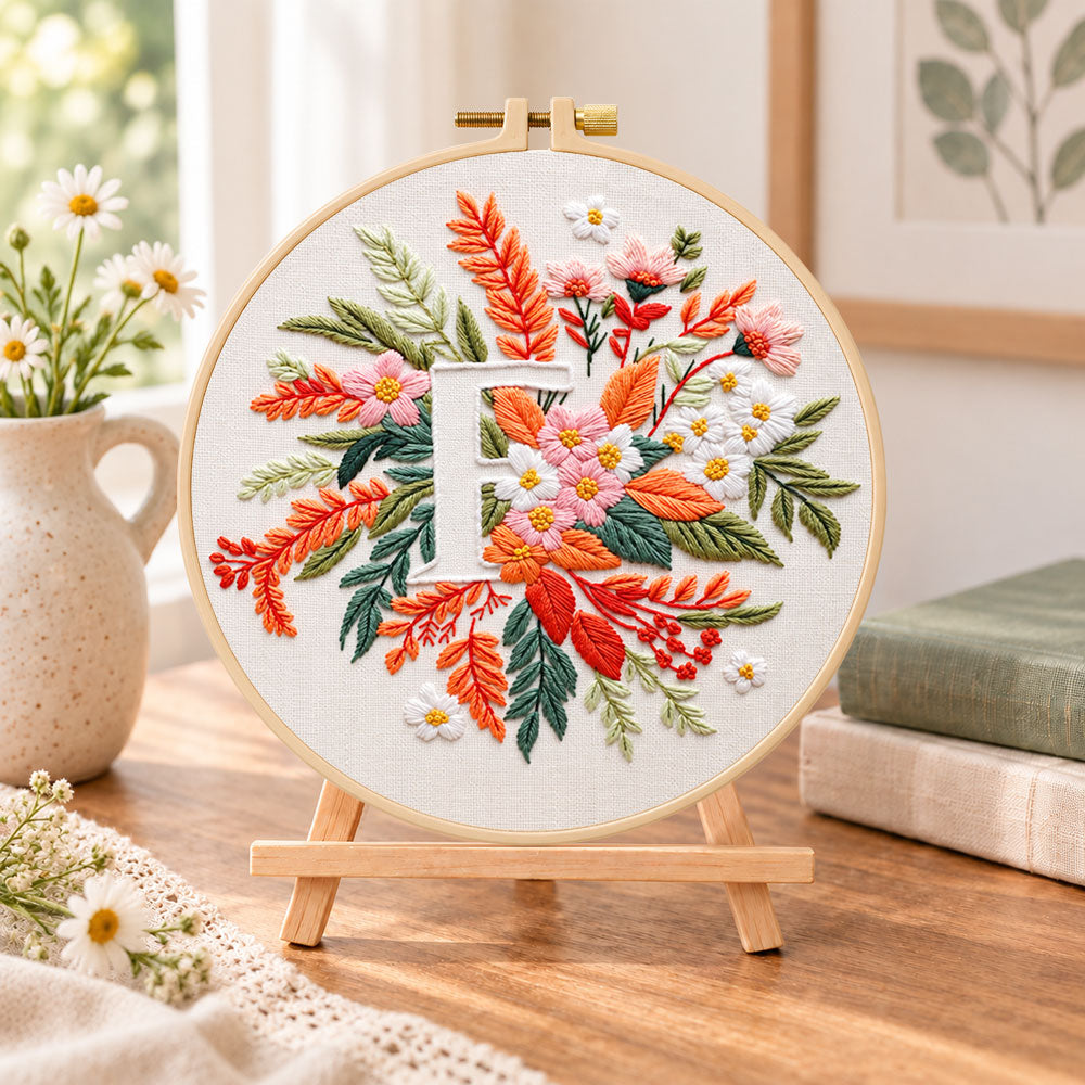 Warm autumn foliage and letter f embroidery kit finished hoop displayed on a wooden stand as cosy tabletop decor