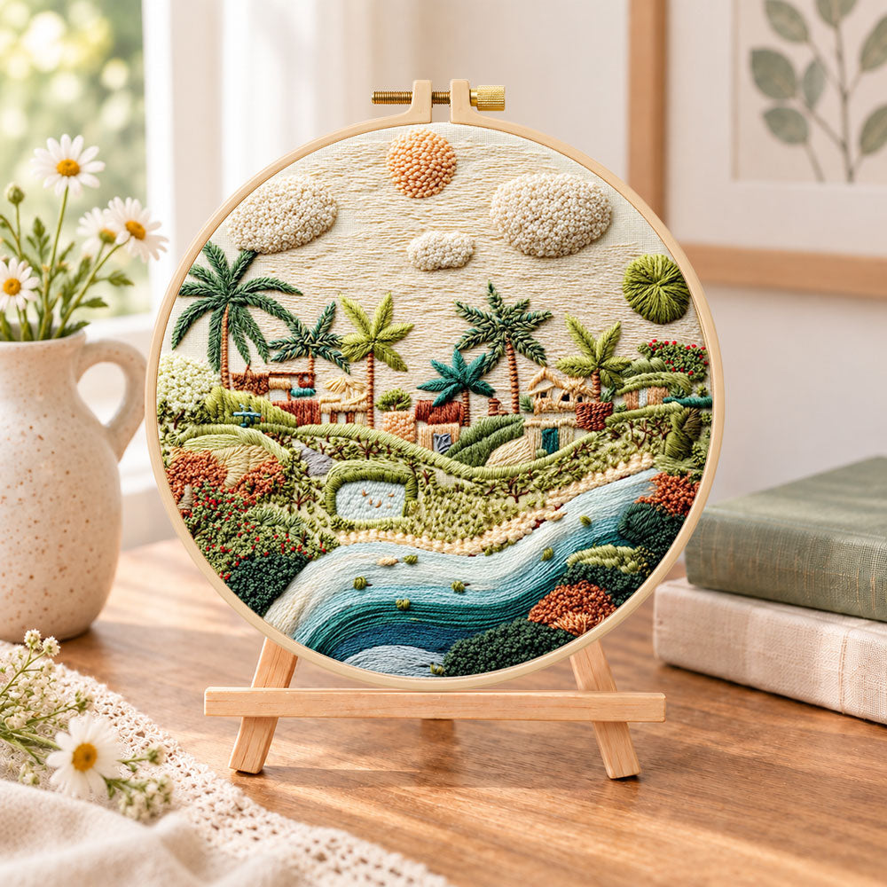 Warm sunlit village embroidery kit finished hoop displayed on a wooden stand as cosy tabletop decor