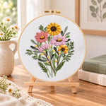 Warm‑toned posy embroidery kit finished hoop displayed on a wooden stand as cozy tabletop decor
