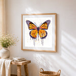 Watercolour butterfly with splatter effect cross stitch artwork displayed on wall as home decor