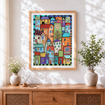 Finished whimsical colourful village cross stitch artwork displayed